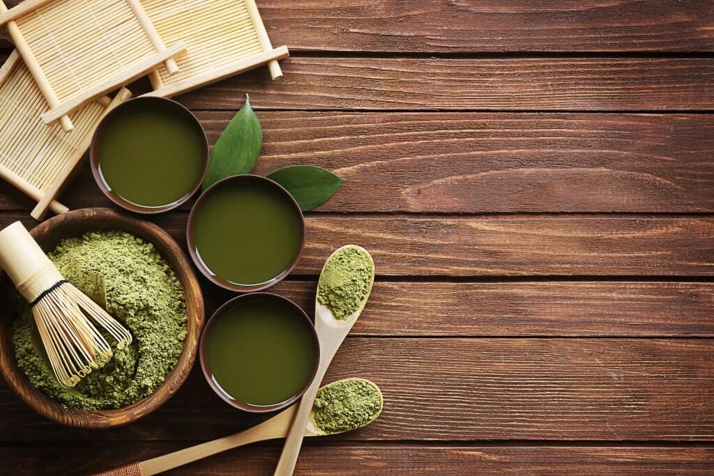 A cup of matcha tea next to a traditional bamboo whisk.