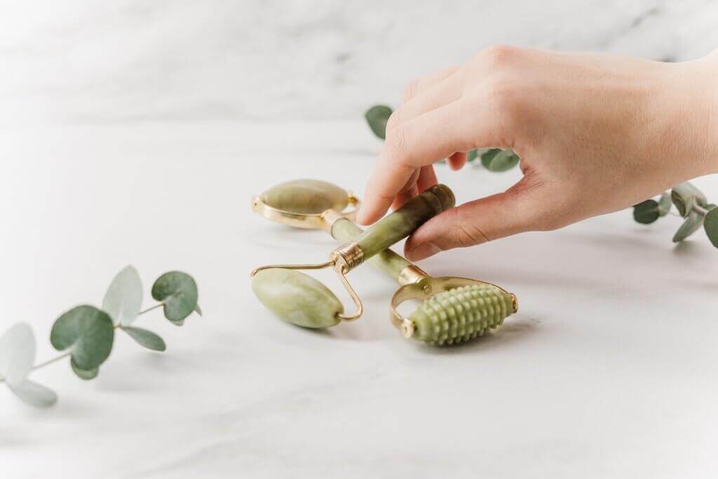 A jade roller and gua sha tool on a white background.