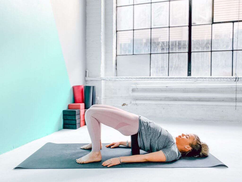 Woman in a relaxing Supported Bridge Pose with a yoga block.
